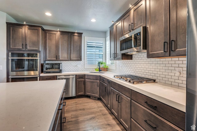 15058 S Spring Canyon Dr, Herriman, UT 84096 - kitchen featuring stainless steel appliances, a sink, dark brown cabinetry, light wood-style flooring, and light countertops