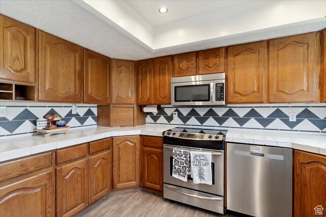 1602 E 2550 N, Layton, UT 84040 - kitchen with appliances with stainless steel finishes, tile countertops, brown cabinets, light wood-style flooring, and recessed lighting