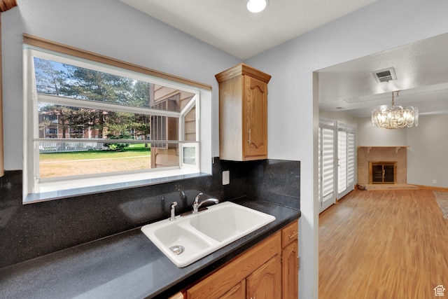 7733 S Briarsprings Dr, Midvale, UT 84047 - kitchen with a sink, dark countertops, light wood-style floors, a chandelier, and a glass covered fireplace