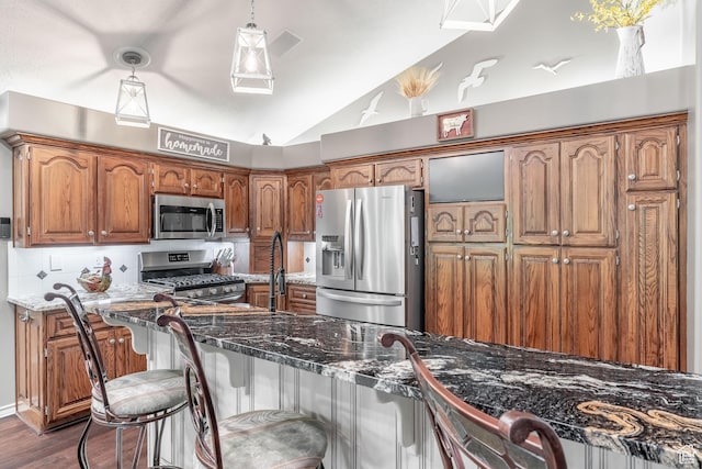 4862 S Kiwana Dr, South Ogden, UT 84403 - kitchen featuring appliances with stainless steel finishes, vaulted ceiling, brown cabinetry, dark wood finished floors, and a breakfast bar