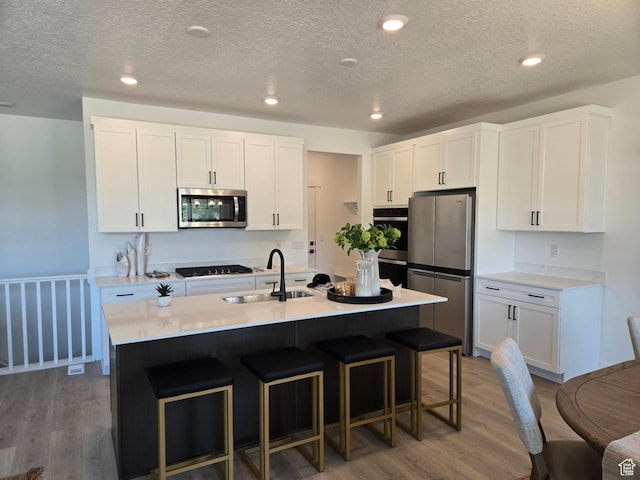 4286 W 1600 S Unit 301, Ogden, UT 84404 - kitchen featuring appliances with stainless steel finishes, wood finished floors, a breakfast bar area, white cabinets, and a textured ceiling