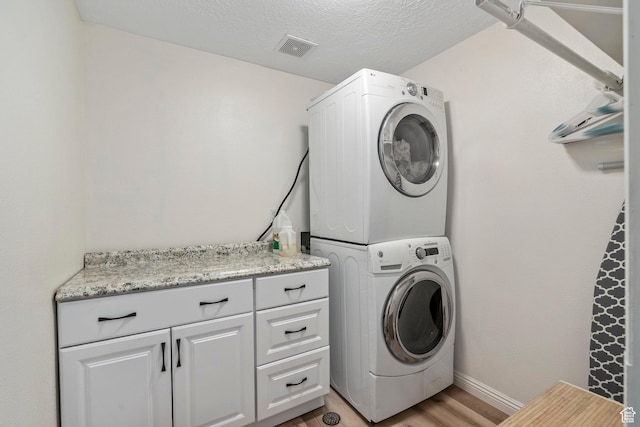 116 S Canyon View Dr, Elk Ridge, UT 84651 - washroom with stacked washing machine and dryer, cabinet space, light wood-style floors, baseboards, and a textured ceiling