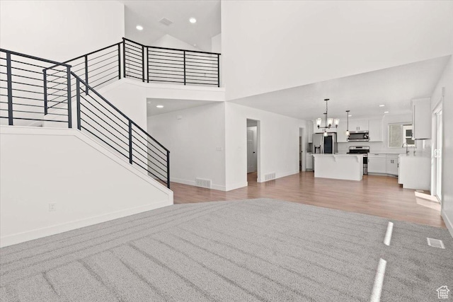 12361 S Xander Ln, Herriman, UT 84096 - unfurnished living room with a chandelier, a high ceiling, baseboards, light colored carpet, and stairs