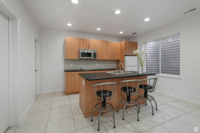 4554 W Birdie Way S, Jordan, UT 84009 - kitchen with stainless steel microwave, a sink, dark countertops, a kitchen island with sink, and light tile patterned floors