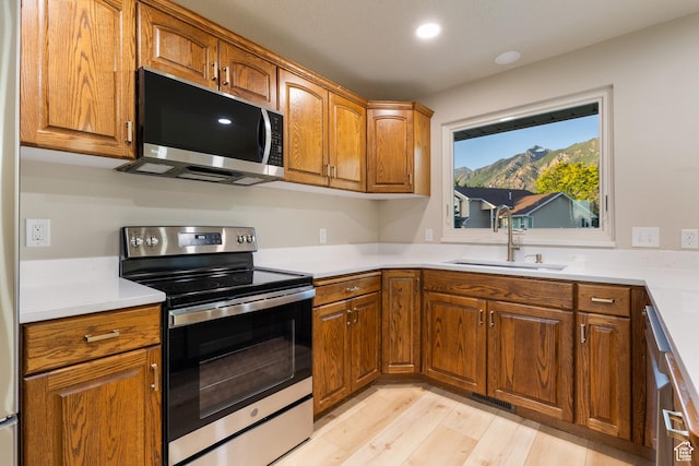 10861 N Panorama Dr, Highland, UT 84003 - kitchen with appliances with stainless steel finishes, a sink, brown cabinetry, light wood-type flooring, and light countertops