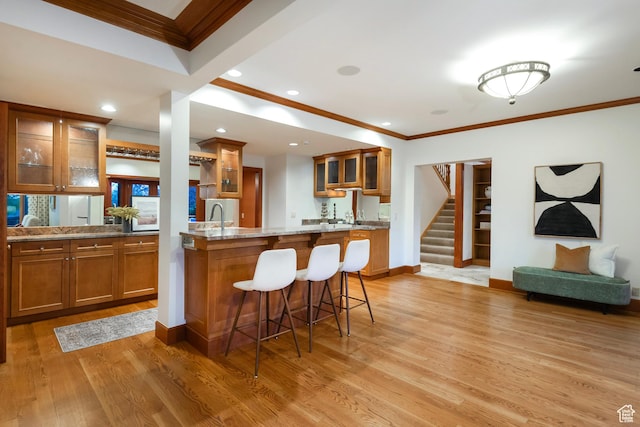 1358 E Tomahawk Dr N, Salt Lake City, UT 84103 - kitchen featuring ornamental molding, brown cabinets, a kitchen bar, light wood finished floors, and glass insert cabinets