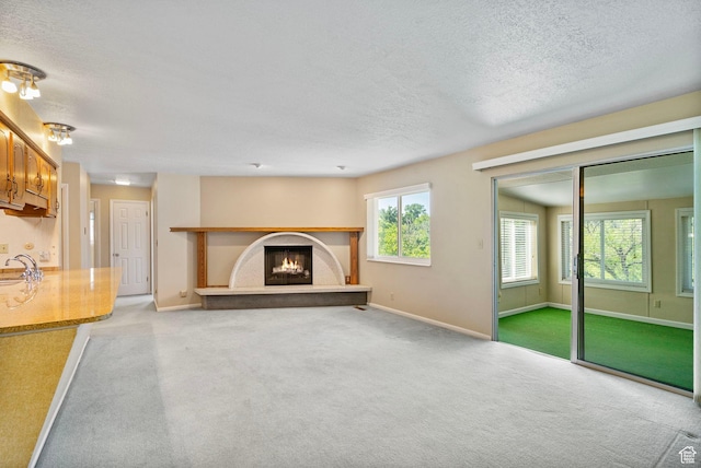 2718 E 200 N, Layton, UT 84040 - unfurnished living room featuring carpet, a textured ceiling, a sink, a warm lit fireplace, and baseboards
