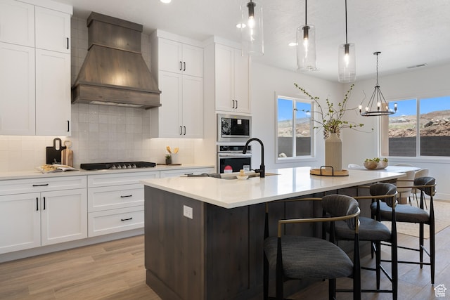 824 S 1690 W, Hurricane, UT 84737 - kitchen featuring custom exhaust hood, backsplash, light wood-style floors, a center island with sink, and light countertops