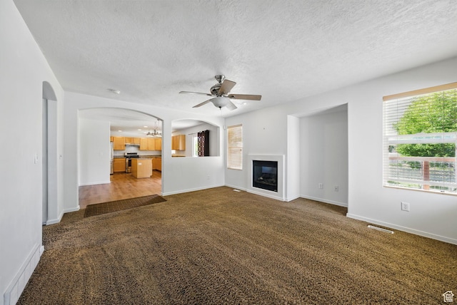 13708 S Manas Ct, Herriman, UT 84096 - unfurnished living room featuring arched walkways, ceiling fan, a textured ceiling, carpet floors, and a glass covered fireplace