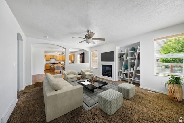 13708 S Manas Ct, Herriman, UT 84096 - living area with arched walkways, a textured ceiling, ceiling fan, a glass covered fireplace, and baseboards