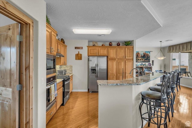 1646 W Sunkissed Dr, St George, UT 84790 - kitchen with appliances with stainless steel finishes, a textured ceiling, a kitchen bar, light wood-style flooring, and baseboards
