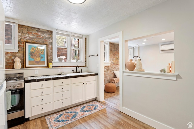 86 B St E Unit 24, Salt Lake City, UT 84150 - kitchen featuring a sink, gas stove, a wall unit AC, tile countertops, and light wood-style flooring