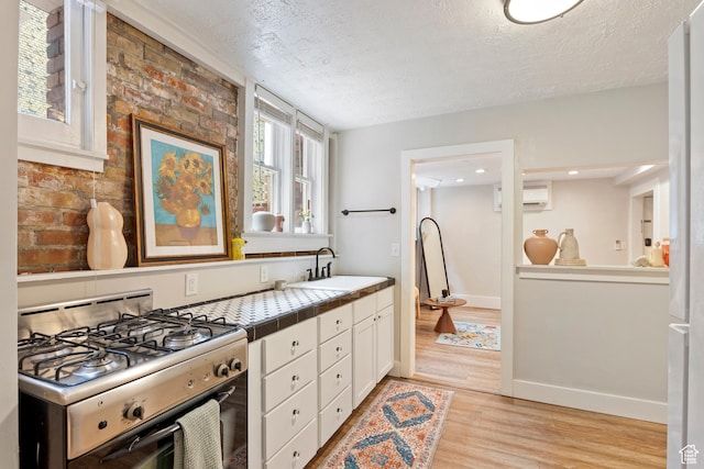 86 B St E Unit 24, Salt Lake City, UT 84150 - kitchen featuring gas stove, tile countertops, a sink, white cabinets, and an AC wall unit