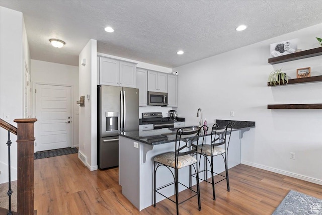 1252 W Cinch Way S, Bluffdale, UT 84065 - kitchen with appliances with stainless steel finishes, a breakfast bar area, wood finished floors, a peninsula, and a textured ceiling