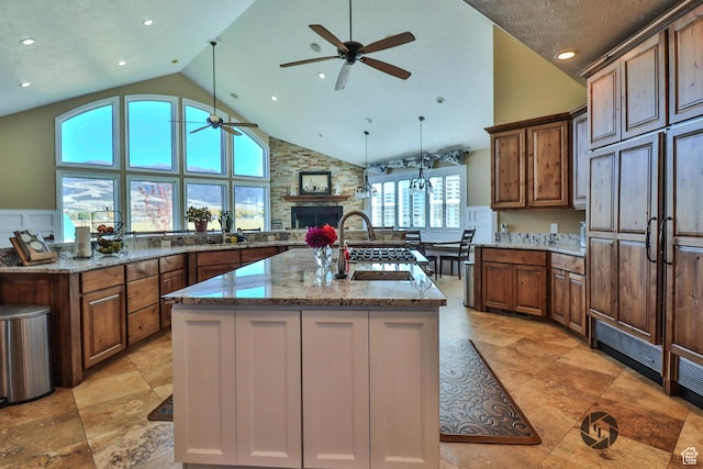 692 E 5020 N, Enoch, UT 84721 - kitchen featuring a ceiling fan, a kitchen island with sink, a fireplace, high vaulted ceiling, and light stone counters