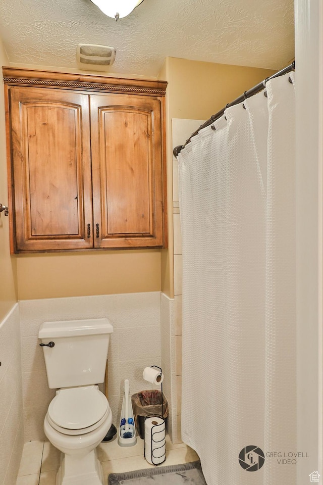 692 E 5020 N, Enoch, UT 84721 - bathroom featuring toilet, a textured ceiling, a wainscoted wall, tile patterned flooring, and tile walls