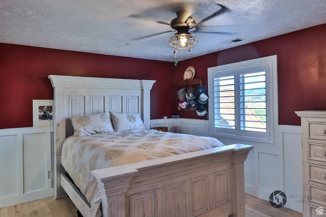 692 E 5020 N, Enoch, UT 84721 - bedroom with light wood-type flooring, wainscoting, a textured ceiling, ceiling fan, and a decorative wall