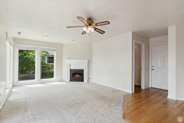 497 E 3525 N, North Ogden, UT 84414 - unfurnished living room featuring ceiling fan, baseboards, a warm lit fireplace, a textured ceiling, and light wood-style flooring