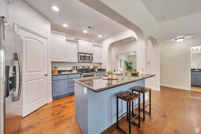 11738 S Currant Dr Unit 112, South Jordan, UT 84009 - kitchen featuring appliances with stainless steel finishes, arched walkways, dark countertops, a breakfast bar area, and light wood-style floors