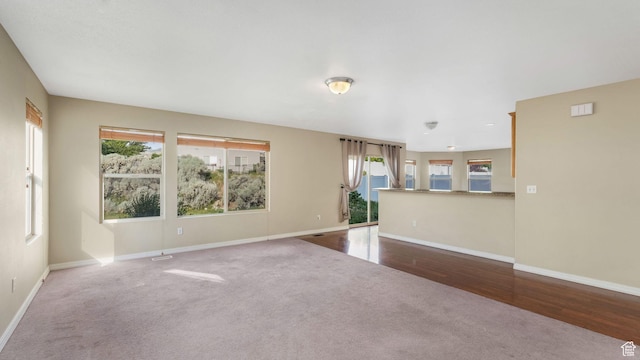 13764 S Rosie Ln, Herriman, UT 84096 - unfurnished living room featuring carpet floors, healthy amount of natural light, baseboards, and wood finished floors