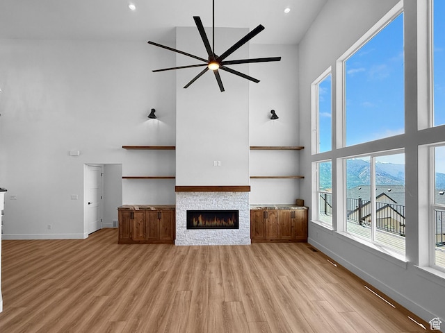 1141 E 4100 N, North Ogden, UT 84414 - unfurnished living room featuring a towering ceiling, ceiling fan, a fireplace, baseboards, and light wood finished floors