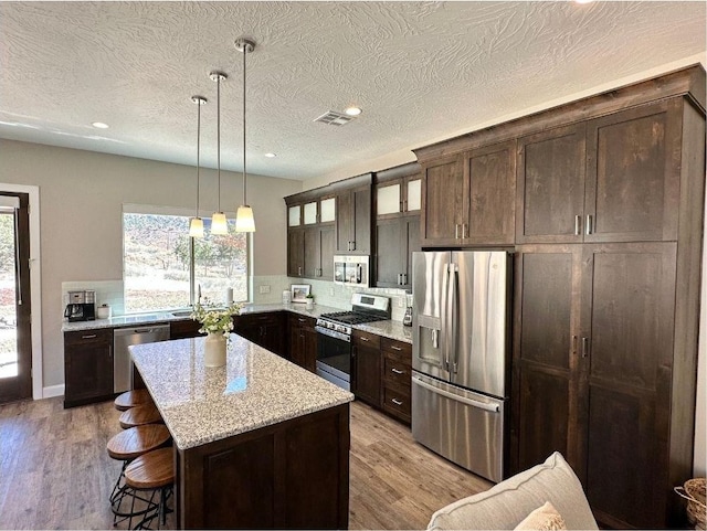 108 Trapper Cir Unit A, Springdale, UT 84767 - kitchen featuring appliances with stainless steel finishes, dark brown cabinetry, glass insert cabinets, tasteful backsplash, and a textured ceiling