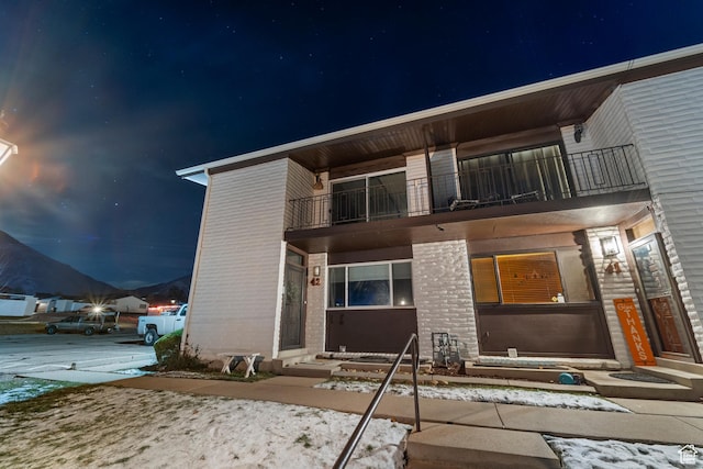 42 Benchmark Vlg, Tooele, UT 84074 - back of house at night featuring entry steps, a balcony, and brick siding