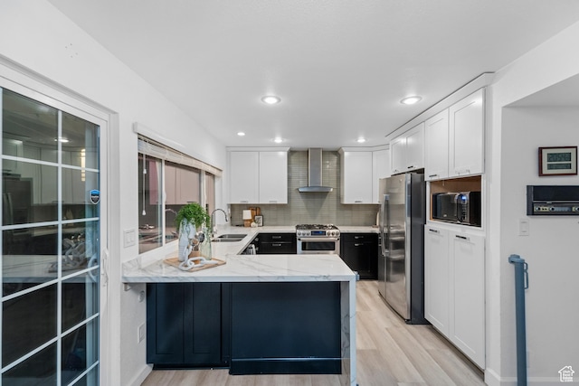 42 Benchmark Vlg, Tooele, UT 84074 - kitchen featuring appliances with stainless steel finishes, wall chimney range hood, a peninsula, light wood finished floors, and white cabinets