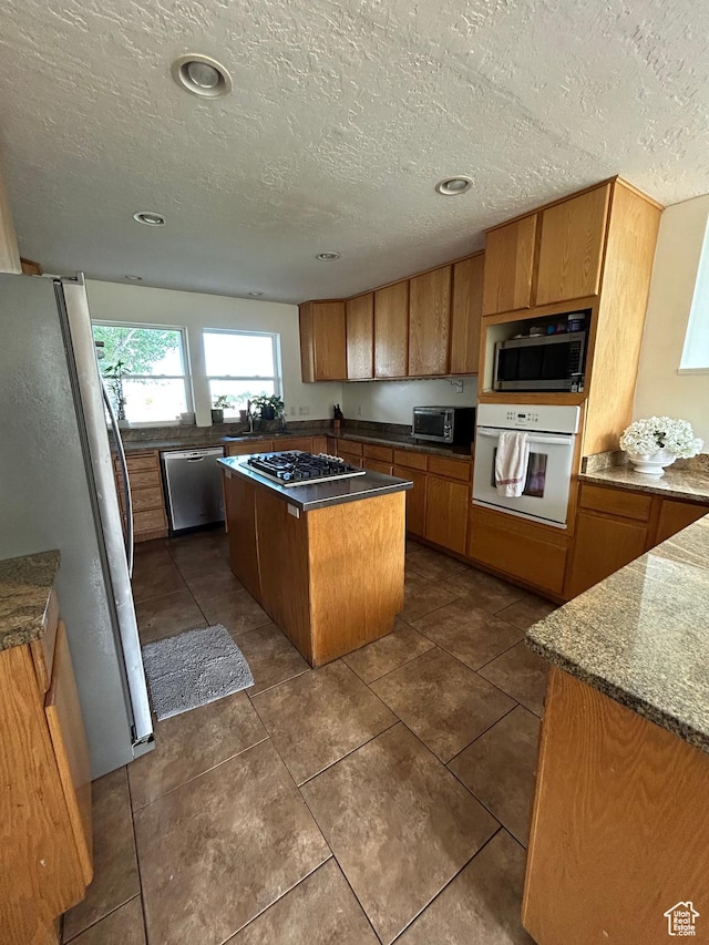 4306 Elk Ln, Erda, UT 84074 - kitchen with appliances with stainless steel finishes, a kitchen island, a textured ceiling, brown cabinets, and a sink