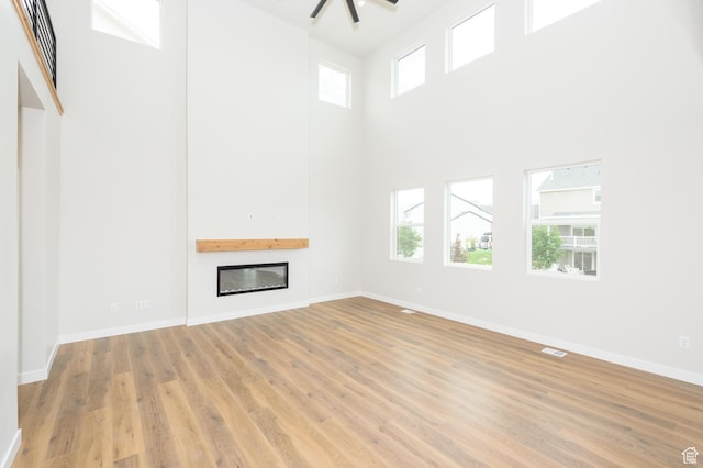 166 N Husker Ln, Saratoga Springs, UT 84045 - unfurnished living room with healthy amount of natural light, a glass covered fireplace, a high ceiling, light wood-style flooring, and baseboards