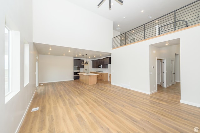 166 N Husker Ln, Saratoga Springs, UT 84045 - unfurnished living room with a towering ceiling, light wood-type flooring, a sink, and baseboards