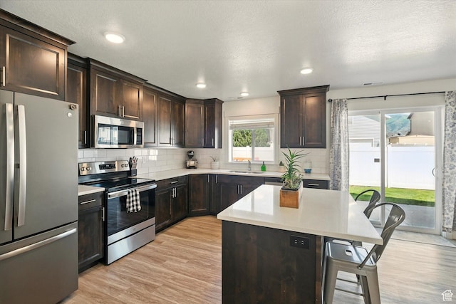 2124 S 1490 W, Wellsville, UT 84339 - kitchen featuring stainless steel appliances, a kitchen breakfast bar, decorative backsplash, light wood-type flooring, and light countertops