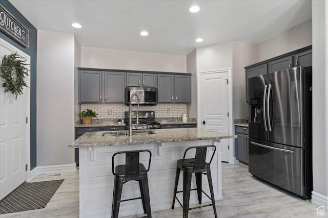 160 S 2875 W, West Point, UT 84015 - kitchen featuring appliances with stainless steel finishes, light stone counters, light wood-type flooring, decorative backsplash, and a kitchen bar