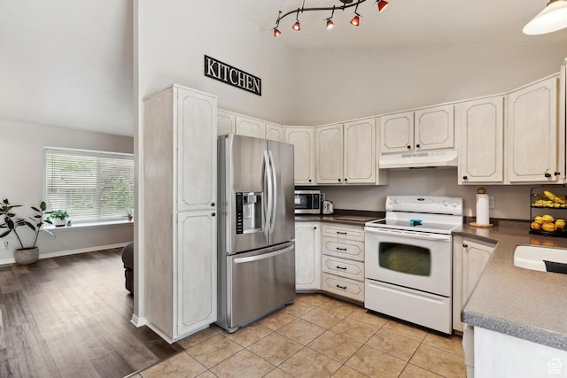 4293 W 5550 S, Roy, UT 84067 - kitchen with appliances with stainless steel finishes, high vaulted ceiling, under cabinet range hood, dark countertops, and light tile patterned floors