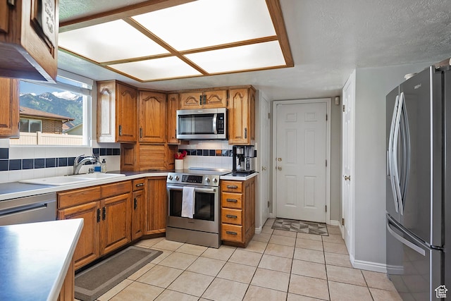 9039 S 1660 E, Sandy, UT 84093 - kitchen with appliances with stainless steel finishes, brown cabinetry, a sink, light tile patterned flooring, and light countertops