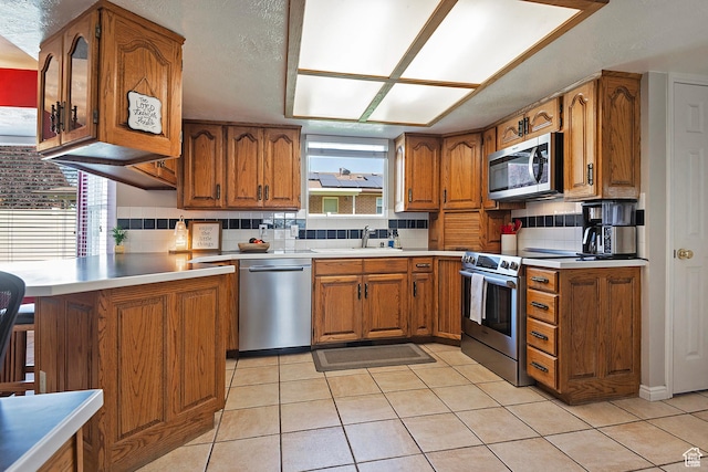 9039 S 1660 E, Sandy, UT 84093 - kitchen featuring stainless steel appliances, brown cabinetry, a peninsula, and light tile patterned floors