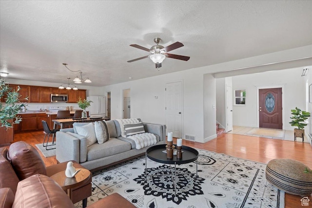 6286 W Anders Ridge Way S, West Valley City, UT 84128 - living room featuring a chandelier, ceiling fan, stairs, light wood-type flooring, and a textured ceiling