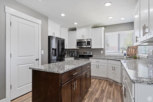 1628 W 1050 S, Syracuse, UT 84075 - kitchen with stainless steel appliances, white cabinetry, dark brown cabinetry, wood finished floors, and light stone countertops