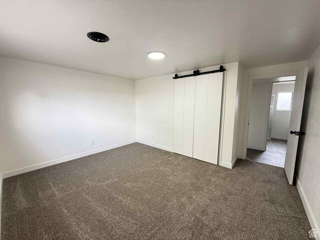 1698 Kenilworth Rd, Helper, UT 84526 - unfurnished bedroom with a barn door, dark carpet, and baseboards