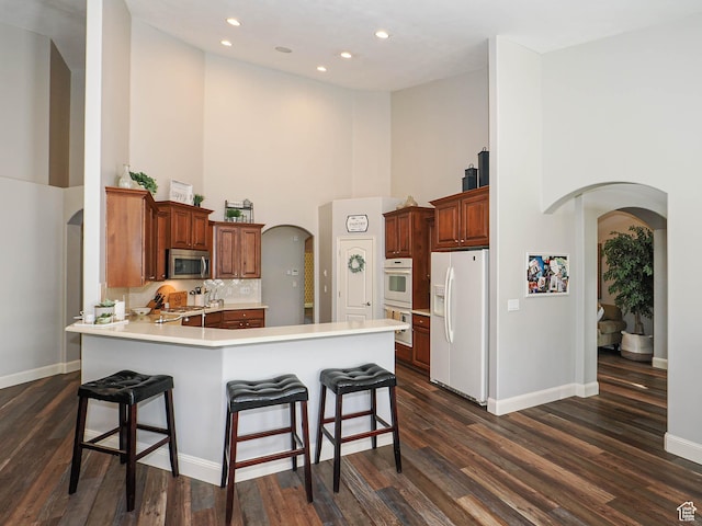 12687 S Verona Creek Way W, Riverton, UT 84065 - kitchen with white fridge with ice dispenser, arched walkways, a high ceiling, stainless steel microwave, and a peninsula