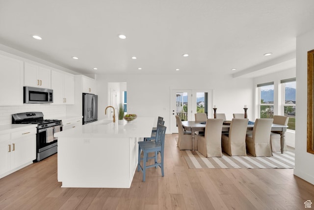 10777 S Lamond Dr W, South Jordan, UT 84009 - kitchen with appliances with stainless steel finishes, a kitchen island with sink, white cabinetry, light countertops, and a kitchen bar