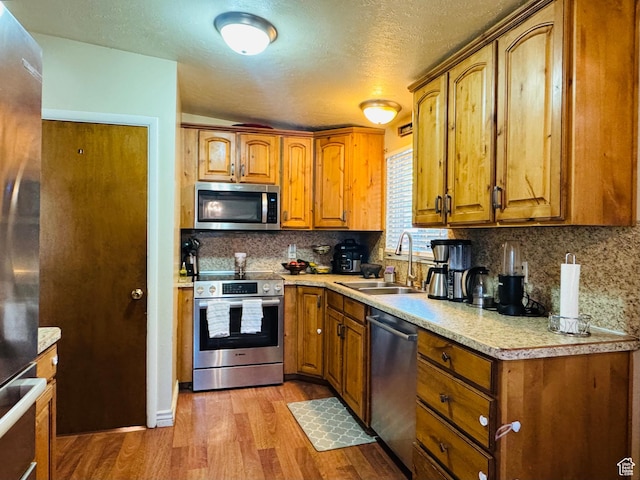 2557 W 5725 S, Roy, UT 84067 - kitchen featuring appliances with stainless steel finishes, a sink, wood finished floors, brown cabinetry, and a textured ceiling