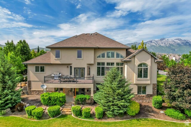 6663 W Normandy Way, Highland, UT 84003 - rear view of property featuring stucco siding, stone siding, a deck with mountain view, a lawn, and roof with shingles