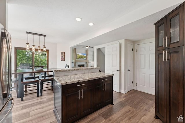 8086 N Meadowview Dr, Snyderville, UT 84098 - kitchen featuring stainless steel fridge, light wood-type flooring, a fireplace, dark brown cabinetry, and a ceiling fan