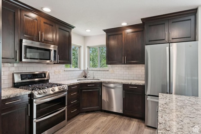 8086 N Meadowview Dr, Snyderville, UT 84098 - kitchen featuring appliances with stainless steel finishes, a sink, light wood-style flooring, tasteful backsplash, and dark brown cabinetry