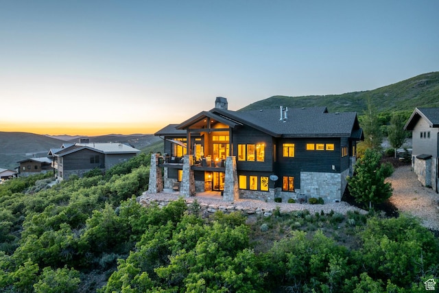1136 E Black Hawk Way, Hideout, UT 84036 - back of property at dusk with a balcony, stone siding, a chimney, and a mountain view