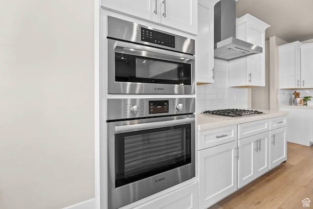 9447 N Arrowhead Dr, Eagle Mountain, UT 84005 - kitchen featuring wall chimney range hood, light countertops, backsplash, white cabinets, and appliances with stainless steel finishes