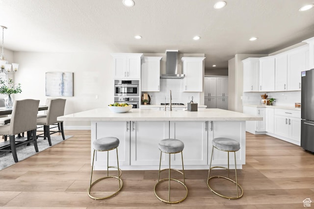 9447 N Arrowhead Dr, Eagle Mountain, UT 84005 - kitchen with wall chimney range hood, stainless steel appliances, recessed lighting, light wood-style flooring, and a kitchen island with sink