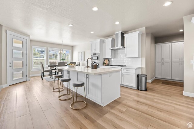 9447 N Arrowhead Dr, Eagle Mountain, UT 84005 - kitchen with wall chimney exhaust hood, baseboards, a kitchen bar, light wood-style flooring, and light countertops