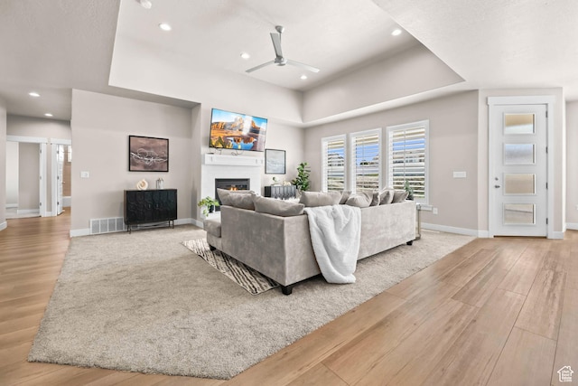 9447 N Arrowhead Dr, Eagle Mountain, UT 84005 - living room featuring a ceiling fan, wood finished floors, a glass covered fireplace, a tray ceiling, and baseboards